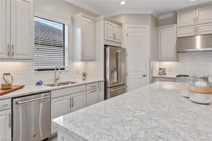 This builder-upgraded extended kitchen features a stylish bar area and casual dining space, complete with a GE Café wine cooler and abundant storage. The glass-front upper cabinets add an elegant touch, perfect for showcasing glassware or decorative pieces, while sliding glass doors provide easy access to the lanai for seamless indoor-outdoor entertaining.