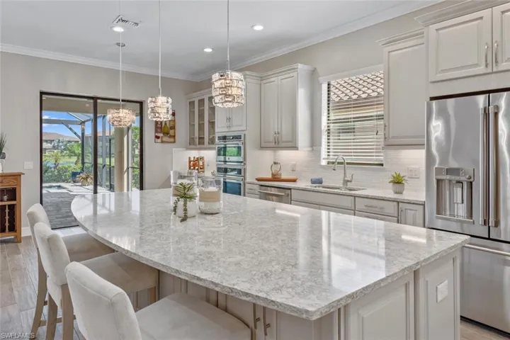 Wood look tile floors, designer lighting fixtures and crown molding in the open concept Kitchen/Great Room/Dining Room/Extended Casual Dining Area with upgraded extended kitchen cabinets & GE Café Wine Cooler
