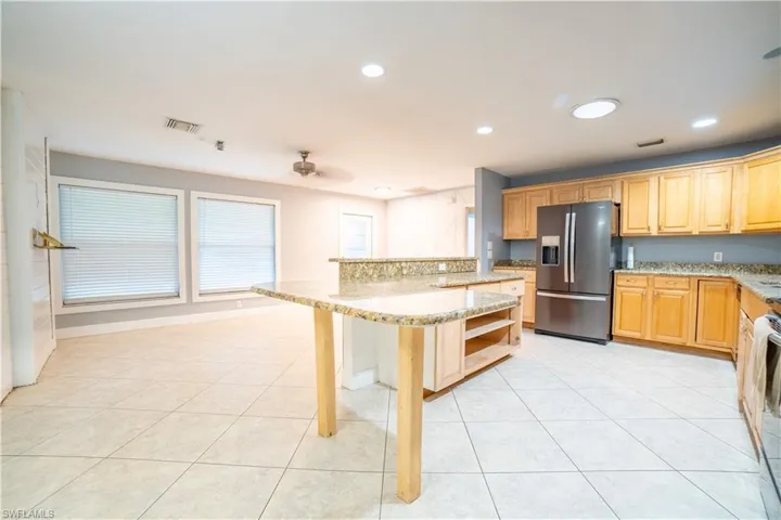 Kitchen featuring a kitchen island, a kitchen breakfast bar, stainless steel appliances, light stone countertops, and light tile patterned floors