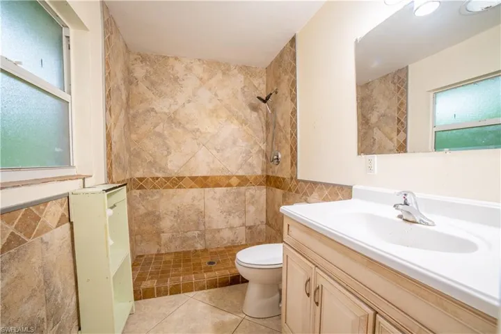 Bathroom featuring vanity, tile walls, toilet, and tiled shower
