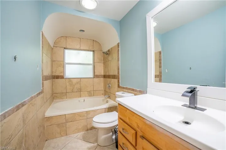 Full bathroom with vanity, tile walls, tiled shower / bath combo, tile patterned floors, and toilet