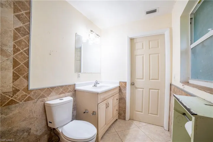 Bathroom featuring tile patterned flooring, toilet, vanity, and tile walls