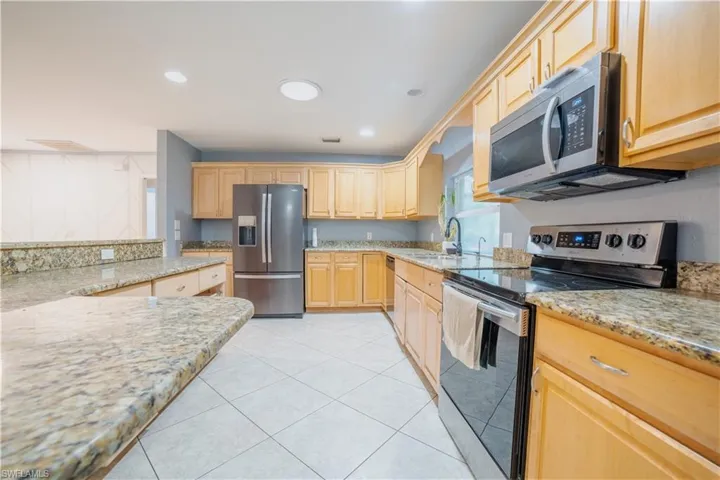 Kitchen featuring a kitchen island, a kitchen breakfast bar, stainless steel appliances, light stone countertops, and light tile patterned floors