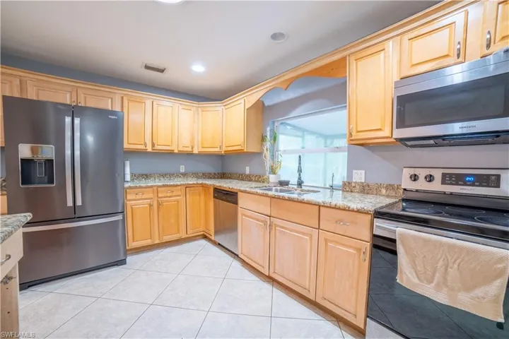 Kitchen featuring light stone countertops, stainless steel appliances, sink, light brown cabinetry, and light tile patterned floors