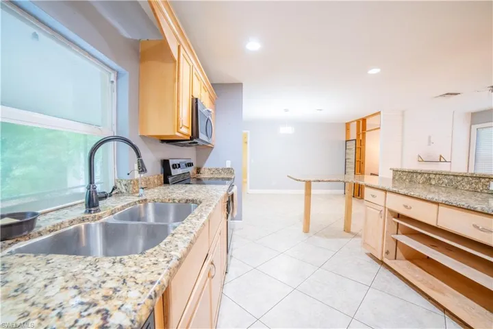 Kitchen with light brown cabinetry, appliances with stainless steel finishes, sink, and light stone counters