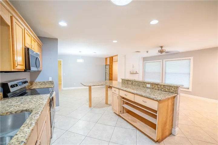 Kitchen featuring light tile patterned flooring, light brown cabinetry, light stone counters, hanging light fixtures, and appliances with stainless steel finishes