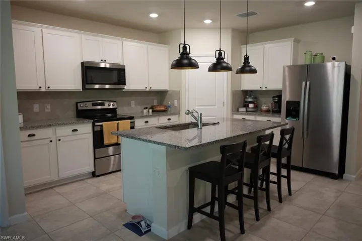 Kitchen with appliances with stainless steel finishes, stone countertops, pendant lighting, white cabinetry, and sink