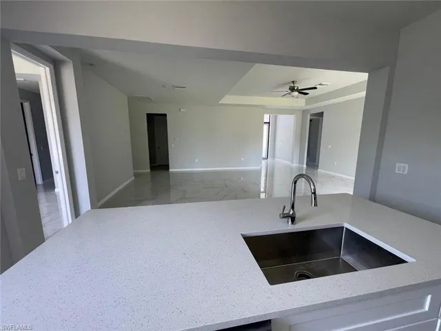 Kitchen with ceiling fan, tile floors, a tray ceiling, light stone countertops, and sink