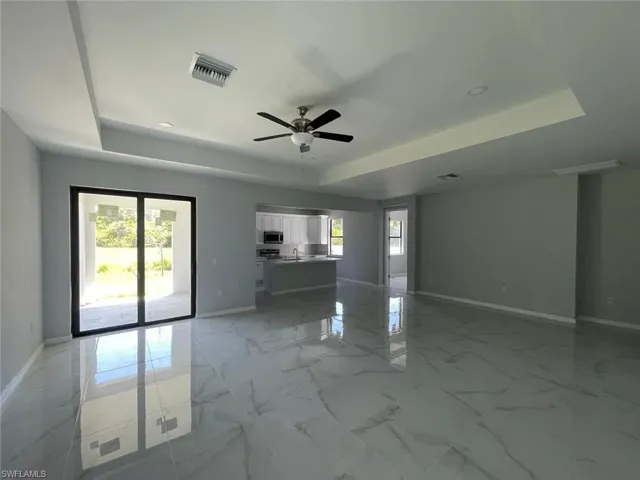 Empty room with a tray ceiling, a healthy amount of sunlight, and light tile floors