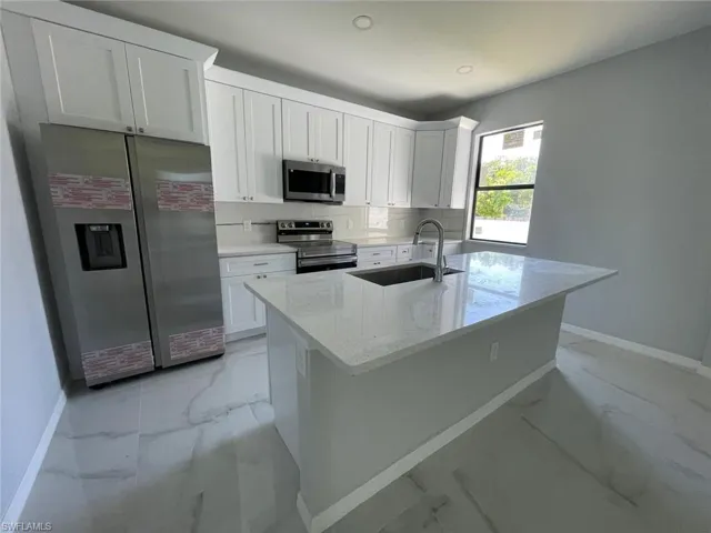Kitchen featuring an island with sink, light tile floors, white cabinetry, and appliances with stainless steel finishes