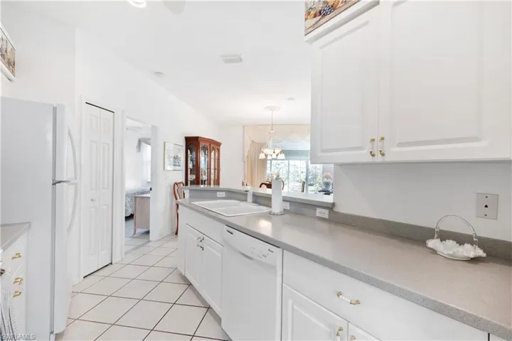 Kitchen with white cabinetry, pendant lighting, white appliances, sink, and light tile patterned floors