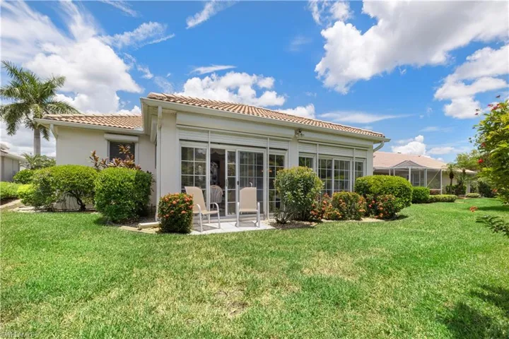 Back of property with a patio area overlooking flowering shrubs and pond