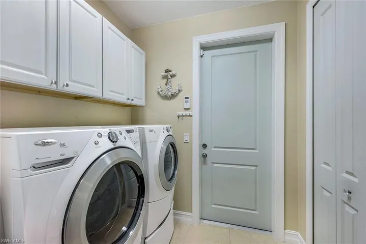 Laundry area with independent washer and dryer, light tile flooring, and cabinets