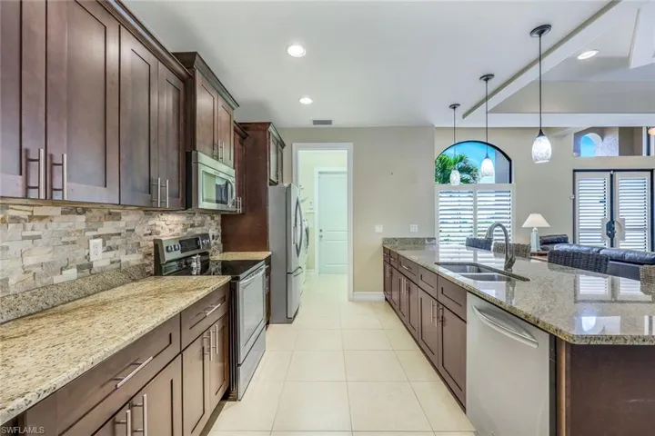 Kitchen featuring light stone countertops, tasteful backsplash, stainless steel appliances, decorative light fixtures, and light tile floors