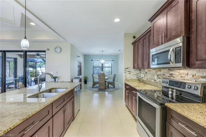 Kitchen with ceiling fan, stainless steel appliances, pendant lighting, light stone counters, and sink