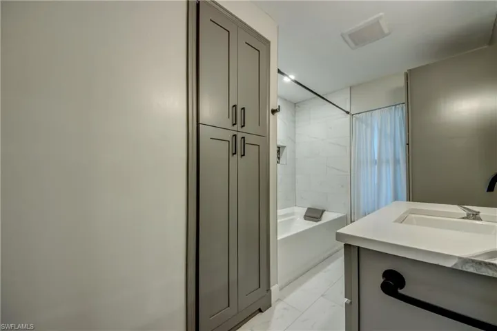 Full bathroom with marble look tile flooring, vanity, and shower / oversize tub combo