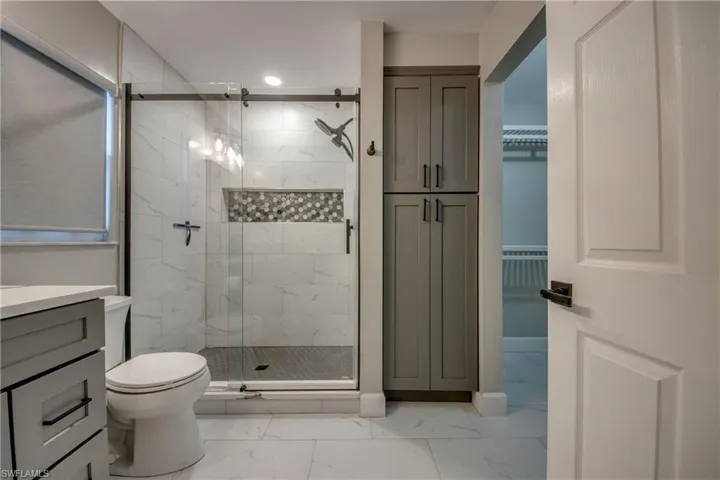 Full bathroom with marble finish flooring, a marble finish shower, toilet, vanity, and a spacious closet