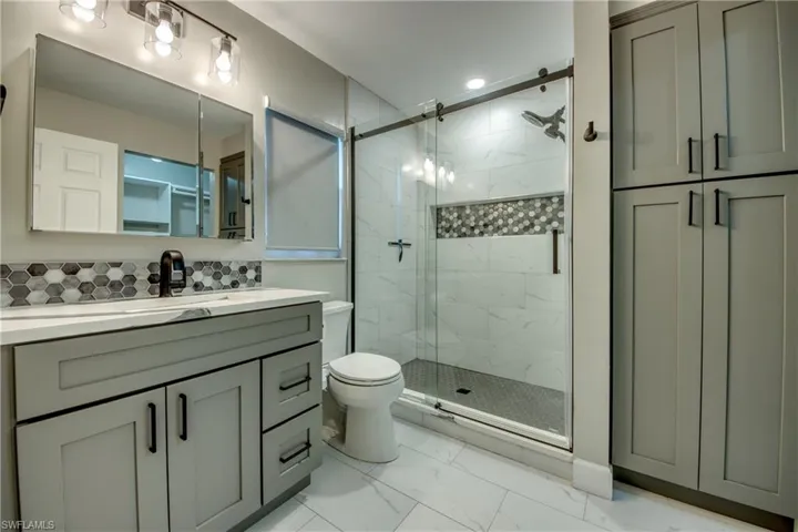 Full bath featuring marble look tiles, a stall shower, vanity, and toilet