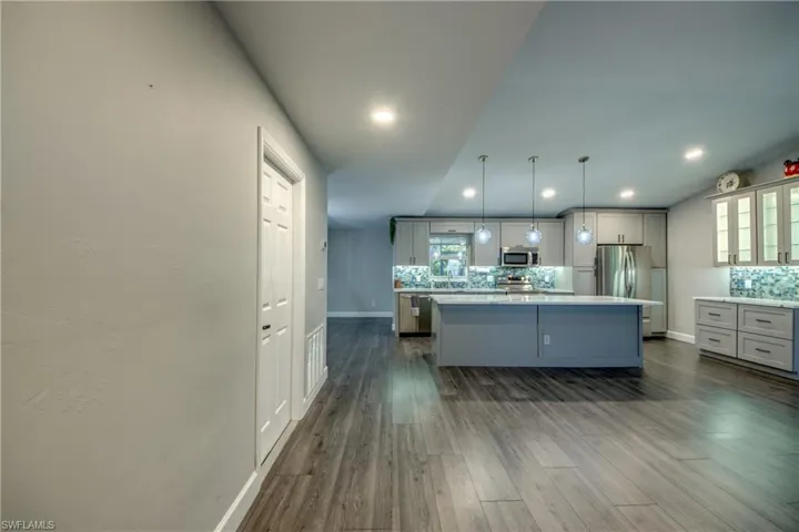 Kitchen with appliances with stainless steel finishes, tasteful backsplash, a kitchen island, baseboards, and dark wood-style flooring