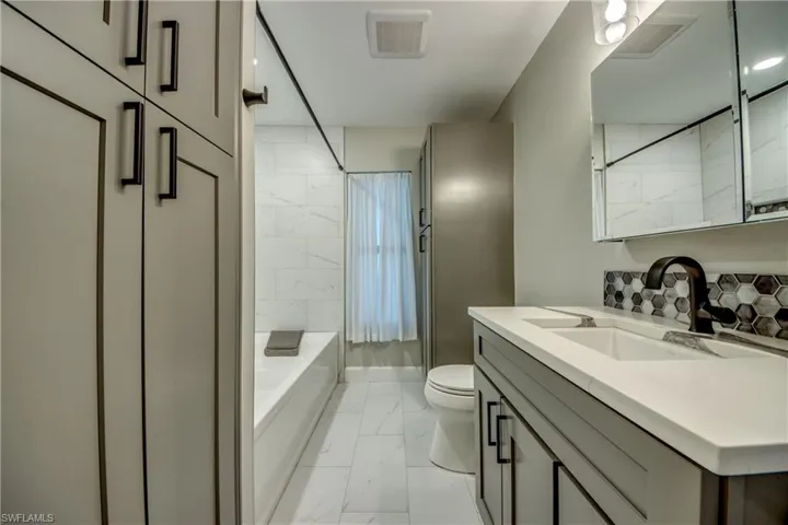 Guest Bathroom featuring marble finish flooring, vanity, toilet, and shower / oversize bathtub combination