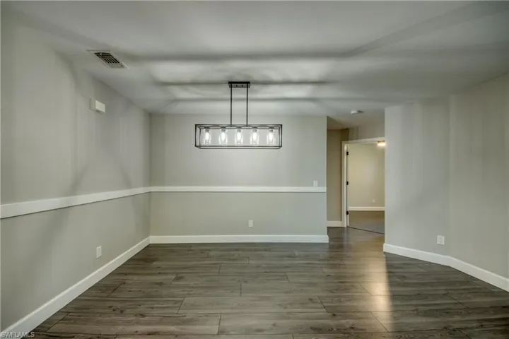 Unfurnished dining area with dark wood-style floors and baseboards