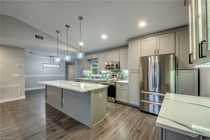 Kitchen featuring stainless steel appliances, a center island, wood finished floors, gray cabinets, and pendant lighting