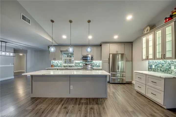 Kitchen with appliances with stainless steel finishes, tasteful backsplash, a center island, wood finished floors, and hanging light fixtures