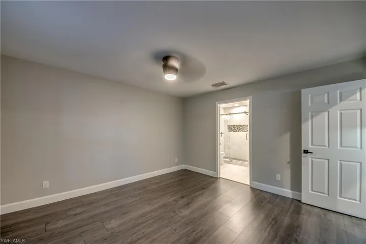 Master bedroom with baseboards, dark wood-style flooring, ensuite bath, and a ceiling fan