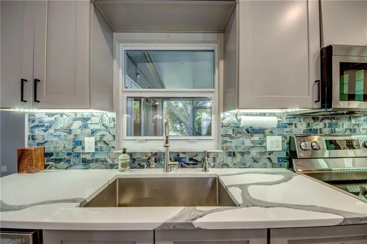 Kitchen with stainless steel microwave, a sink, decorative backsplash, and light stone countertops