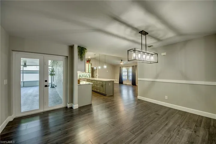Unfurnished living room featuring dark wood finished floors, french doors, baseboards, and a chandelier