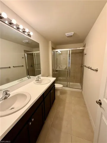 Bathroom with double vanity, a stall shower, and light tile patterned floors