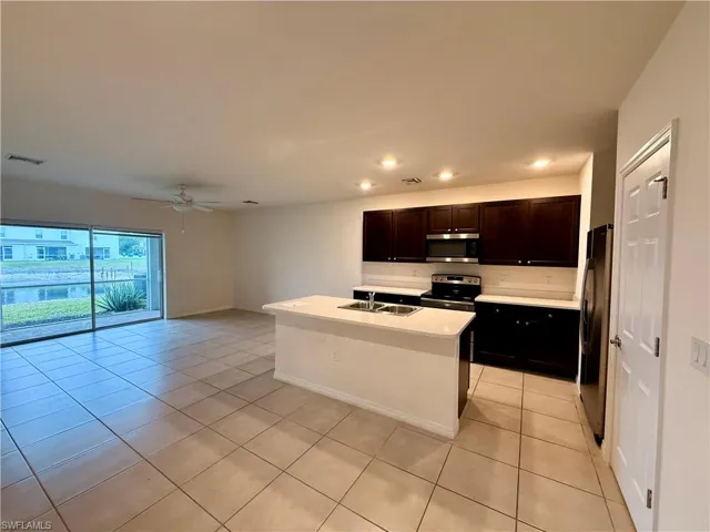 Kitchen with a center island with sink, stainless steel appliances, light tile patterned floors, ceiling fan, and dark brown cabinets