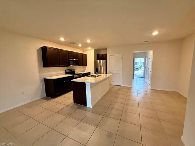 Kitchen with stainless steel appliances, a center island with sink, light tile patterned flooring, recessed lighting, and dark brown cabinetry