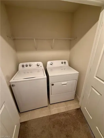 Laundry area with washing machine and dryer, light tile patterned floors, and light colored carpet
