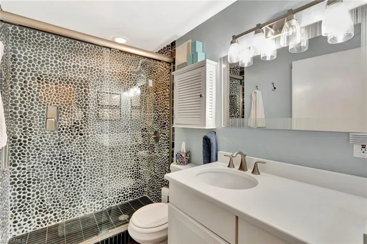 Full bath with a large pebbled shower & shiny glass doors