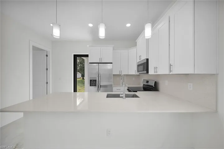 Kitchen featuring white cabinets, stainless steel appliances, light stone countertops, a peninsula, and recessed lighting