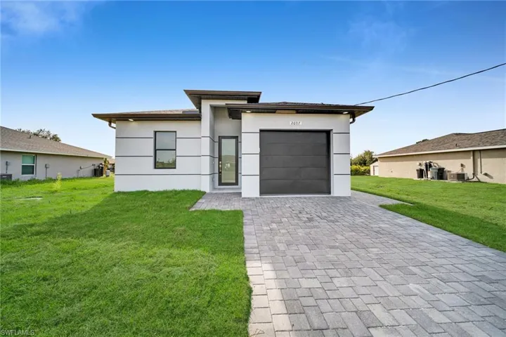 View of front of property with a front yard, decorative driveway, stucco siding, and an attached garage