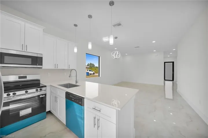 Kitchen featuring appliances with stainless steel finishes, white cabinetry, recessed lighting, decorative light fixtures, and light stone counters