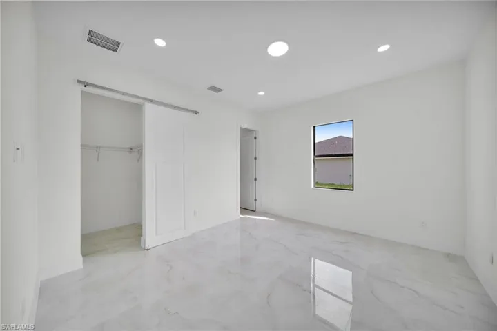 Unfurnished bedroom featuring a barn door, light marble finish flooring, a walk in closet, and recessed lighting