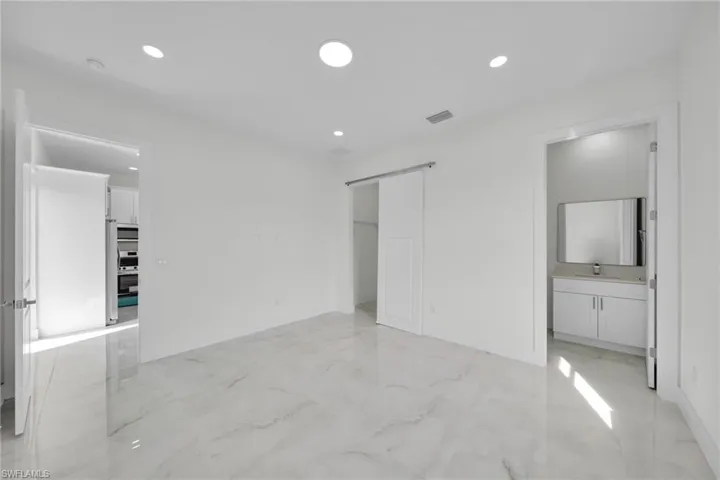 Unfurnished bedroom with light marble finish floors, a barn door, a closet, recessed lighting, and ensuite bath