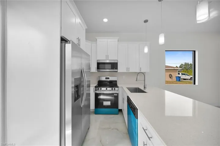 Kitchen featuring appliances with stainless steel finishes, white cabinets, light stone counters, hanging light fixtures, and recessed lighting