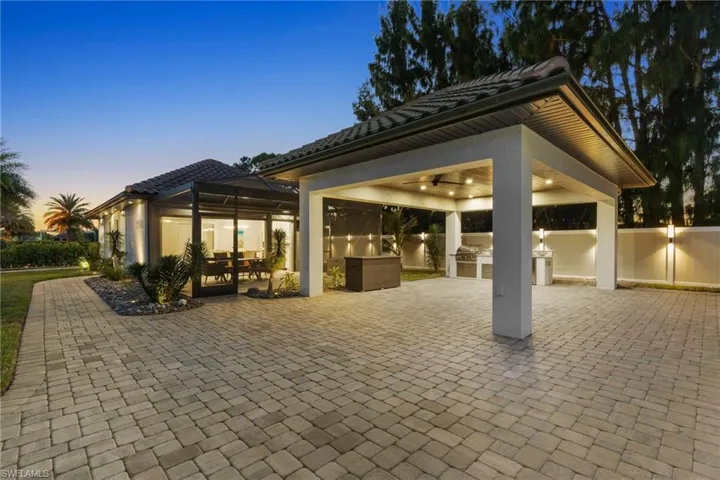 Patio terrace at dusk featuring an outdoor kitchen, ceiling fan, glass enclosure, and a patio area