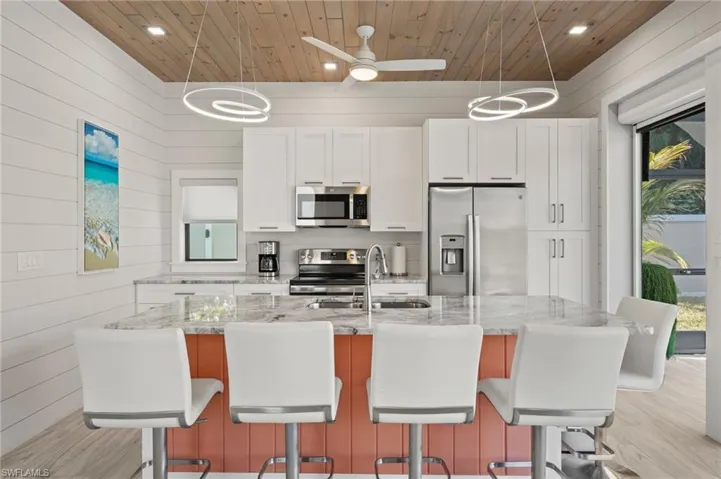 Kitchen featuring appliances with stainless steel finishes, white cabinets, plenty of natural light, light stone countertops, and wooden walls