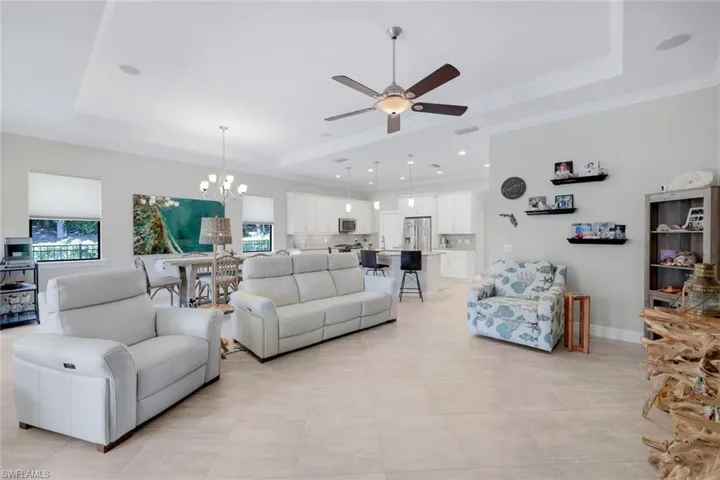 Tiled living room with ceiling fan with notable chandelier, crown molding, and a tray ceiling