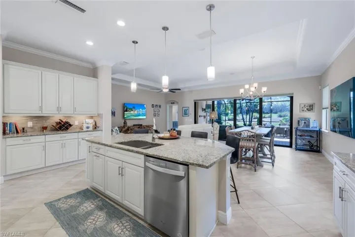 Kitchen with ceiling fan, dishwasher, light stone countertops, a center island with sink, and white cabinets