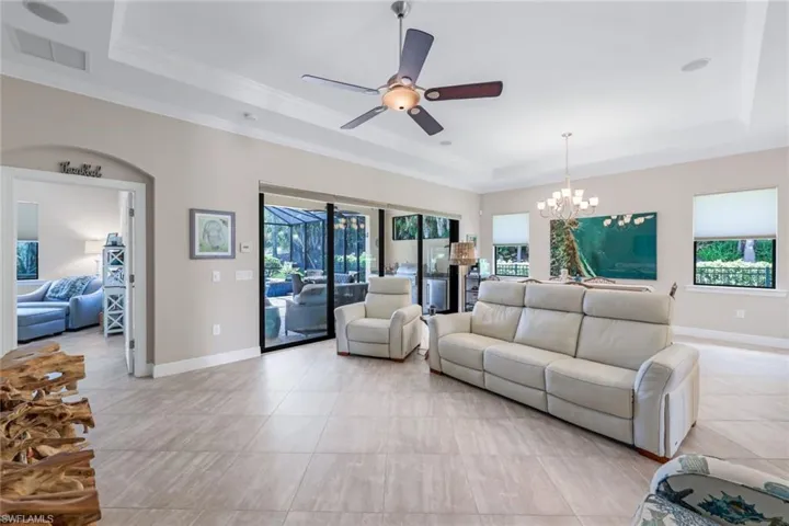 Tiled living room with ceiling fan with notable chandelier, a raised ceiling, and crown molding