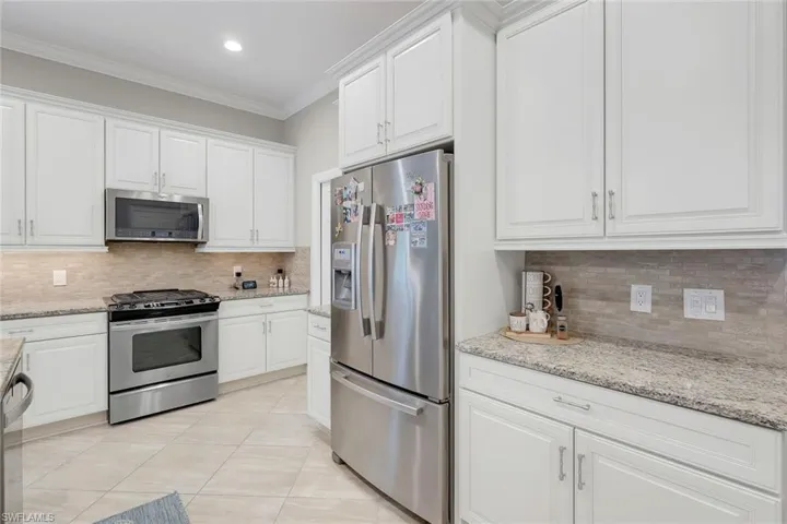 Kitchen featuring crown molding, white cabinetry, stainless steel appliances, light stone countertops, and decorative backsplash