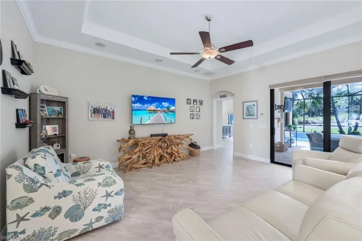 Living room with a tray ceiling, ceiling fan, light tile patterned floors, and crown molding
