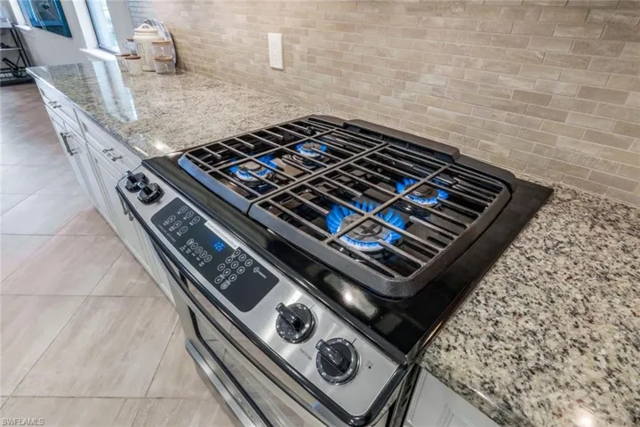 Gas stove, light tile patterned floors, and light stone countertops