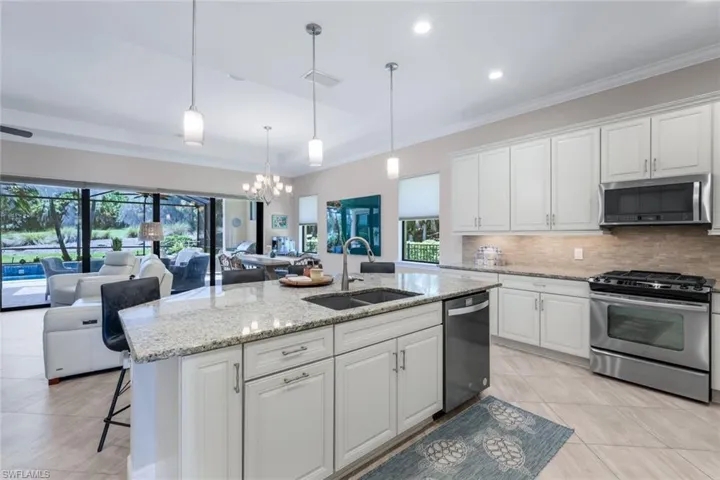 Kitchen featuring a center island with sink, stainless steel appliances, pendant lights and white cabinets